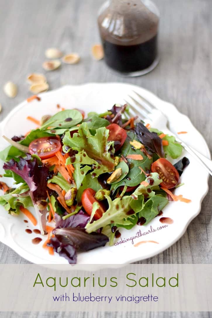 a tossed Aquarius Salad with Blueberry Vinaigrette on a white plate with a bottle of dressing in the background
