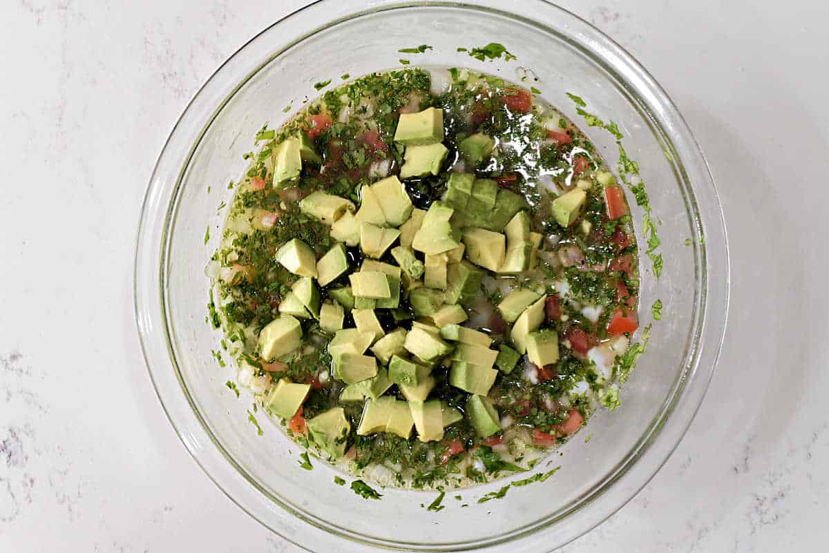 Avocado chunks on top of the chilled shrimp ceviche in a glass bowl.
