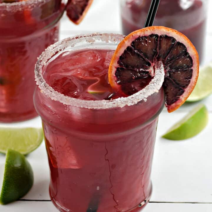 Two blood orange margaritas in short glasses garnished with an orange wheel and a sugar rim.
