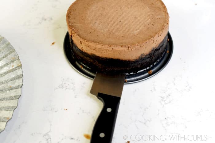 Chef knife running under the cheesecake to lift off the pan base.