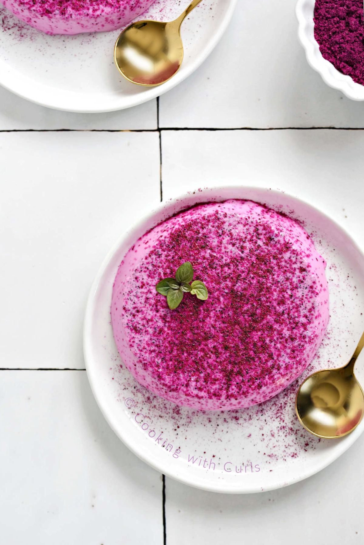 Looking down on a small plate with a pink colored panna cotta topped with a mint leaf.
