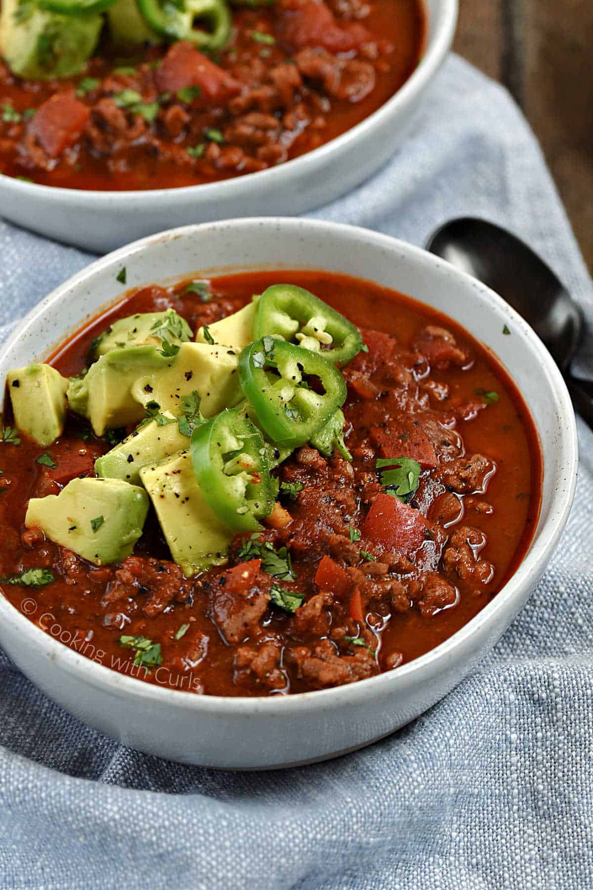 A bowl of bean-free chili in a bowl topped with avocado chunks and sliced jalapenos.