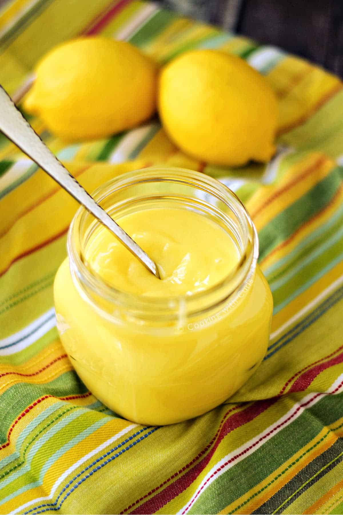 A jar of homemade lemon curd with fresh lemons in the background.