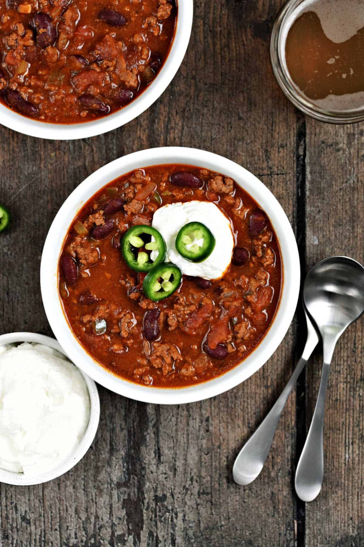 Two bowls of chili topped with sour cream and sliced jalapeños.