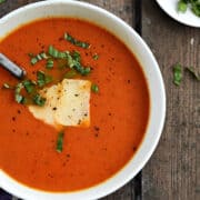 Looking down on a bowl of tomato soup topped with shaved parmesan and shredded basil.