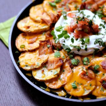Thinly sliced potatoes arranged in a cast iron skillet topped with melted cheese, bacon, sour cream, salsa and green onions.
