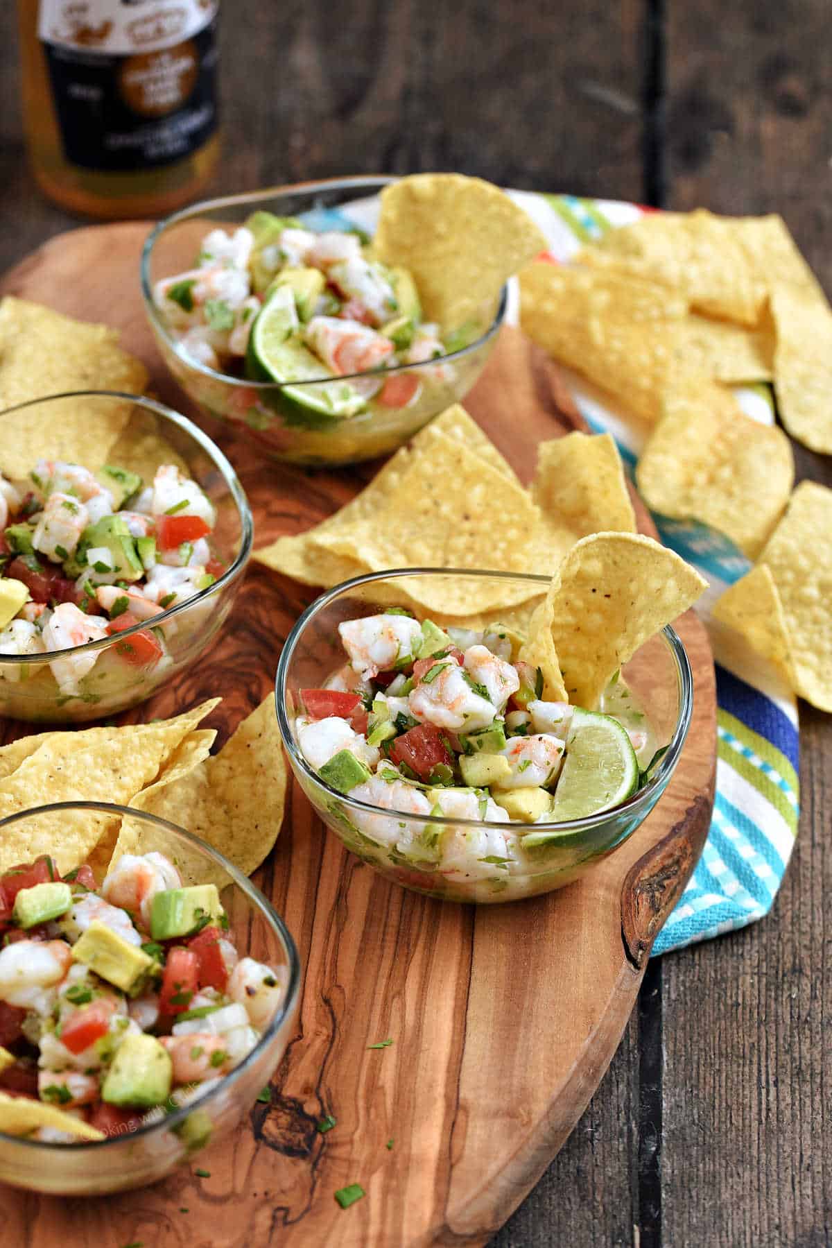 Shrimp, tomato, avocado, and peppers in small bowls surrounded by tortilla chips.