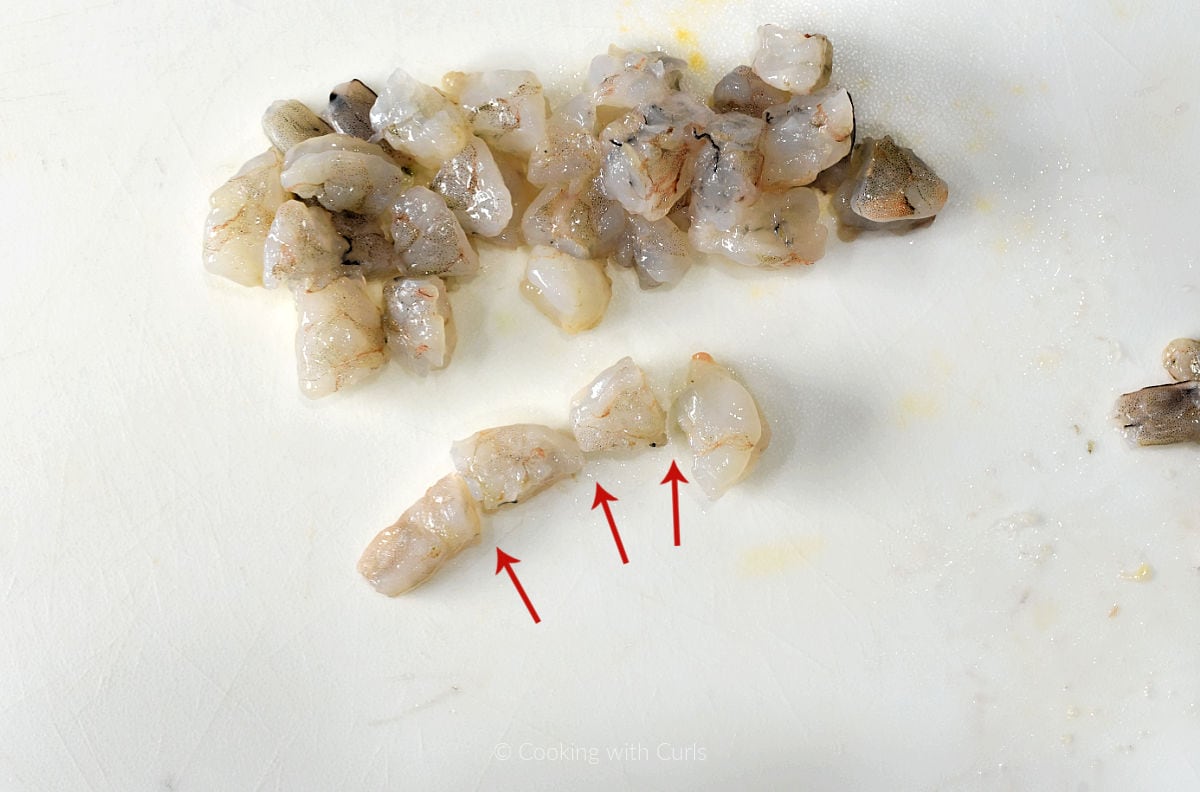 Raw shrimp cut into four pieces on a cutting mat.