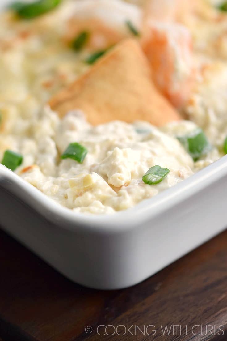 Seafood Artichoke Dip in a white baking dish with a chip sticking out of the top.