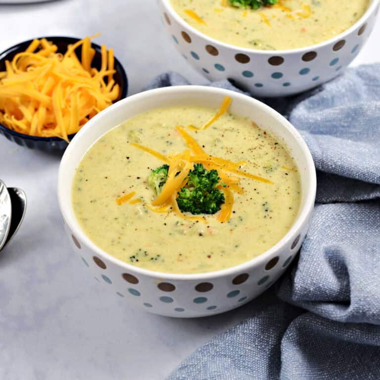 Two bowls of broccoli cheddar soup topped with broccoli and grated cheddar cheese.