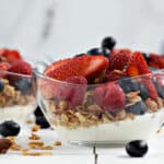 Greek yogurt, granola, fresh raspberries, strawberries and blueberries layered in small glass bowls.