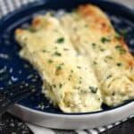 Two Chicken Alfredo Stuffed Manicotti on a dark blue plate.